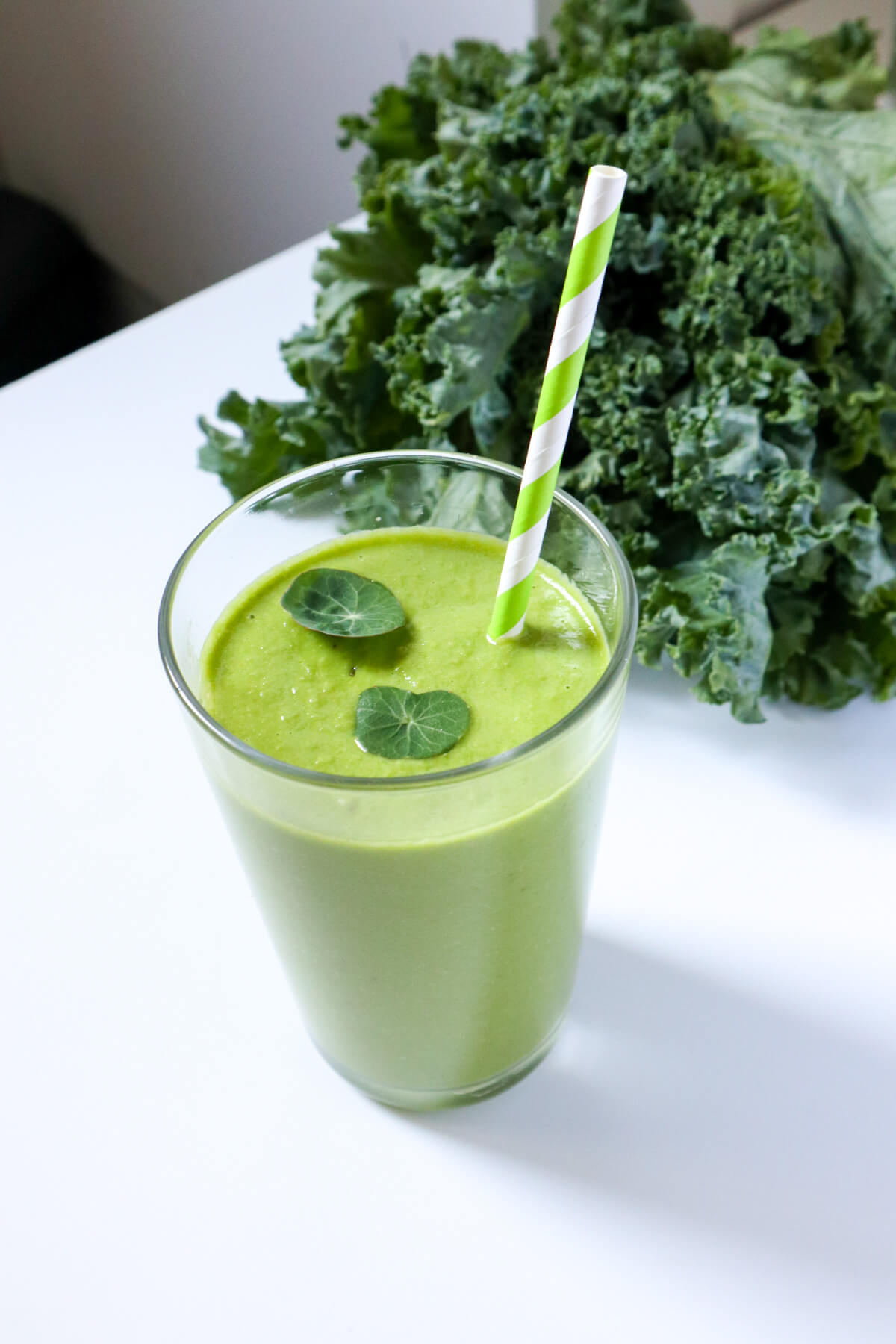 Green smoothie with straw and raw kale in the background. 