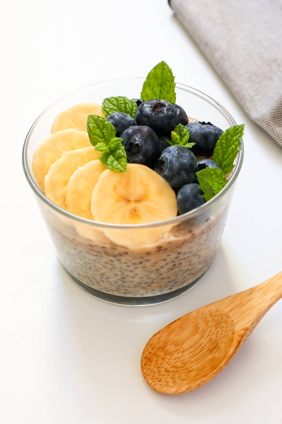 healthy banana chia pudding topped with mint leaves, banana slices and blueberries