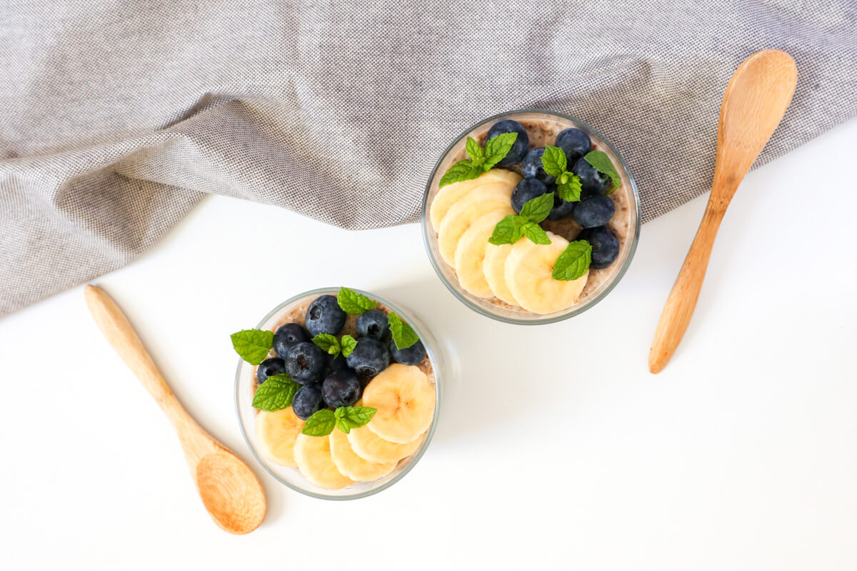 landscape image, 2 chia puddings with grey tablecloth and wooden spoons