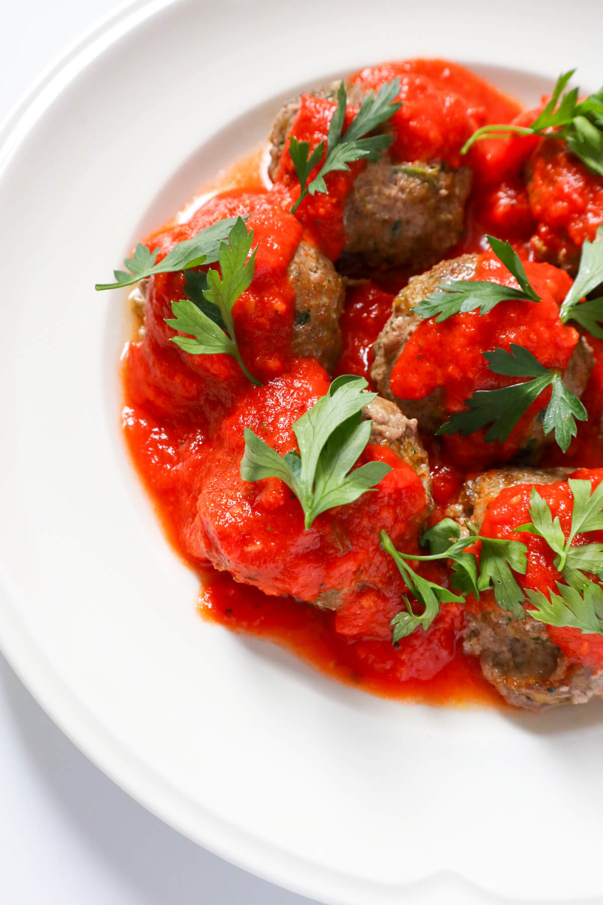 images of half a plate full of meatballs covered in marinara sauce. 