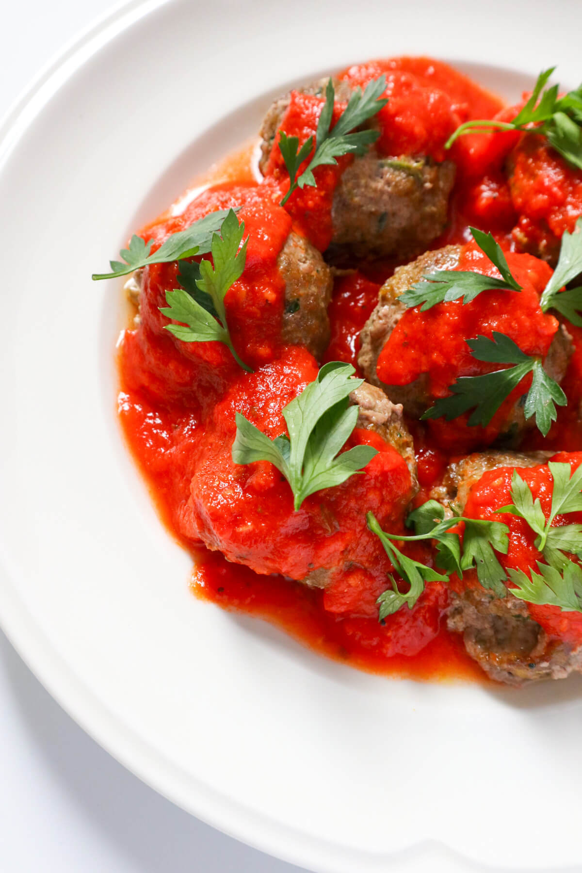 images of half a plate full of meatballs covered in marinara sauce.