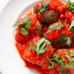 Meatballs covered with marinara sauce and parsley leaves.