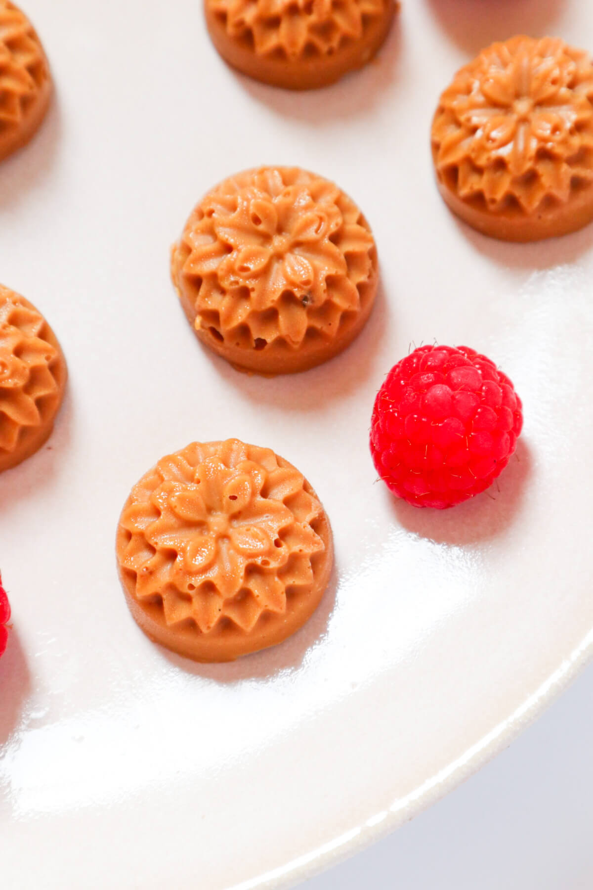 Close up of fat bombs that came out of a flower mold on a plate with a raspberry next to it 