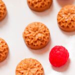 Close up of fat bombs that came out of a flower mold on a plate with a raspberry next to it