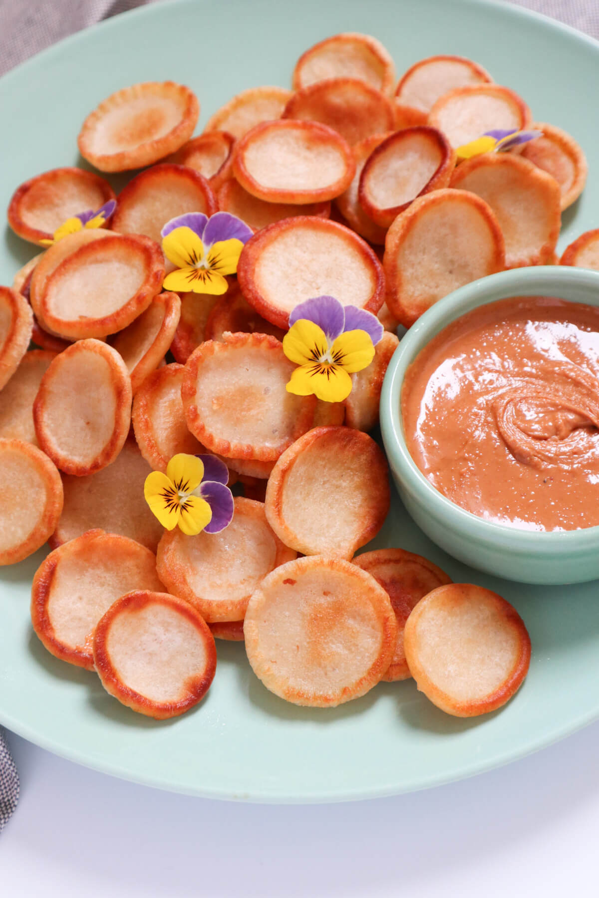 lots of mini pancakes on a plate with peanut butter in a small bowl next to them 