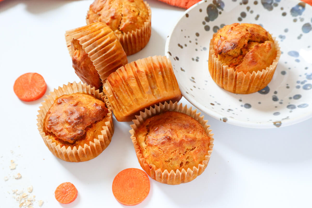 Banana carrot muffins in mufifn cups on white background and a plate withd dots