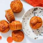Banana carrot muffins in mufifn cups on white background and a plate withd dots
