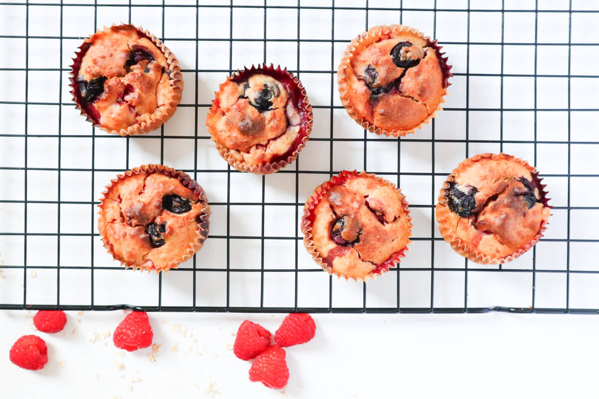 6 muffins on a cookie sheet with raspberries on the side