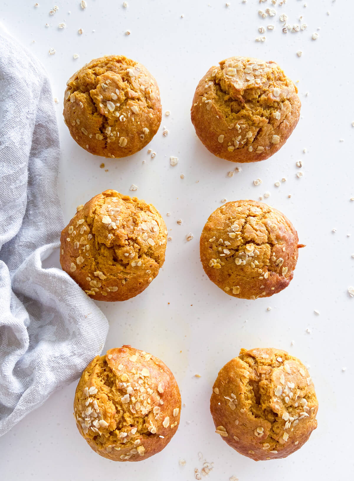6 Pumpkin banana muffins on white background with tablecloth on the right side.