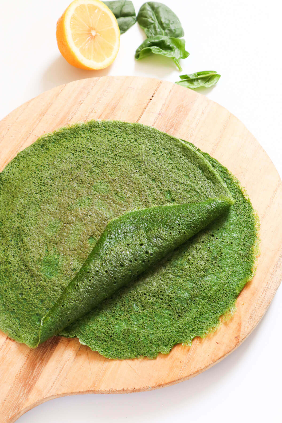 Stack of spinach wraps on a wooden board with one folded over.