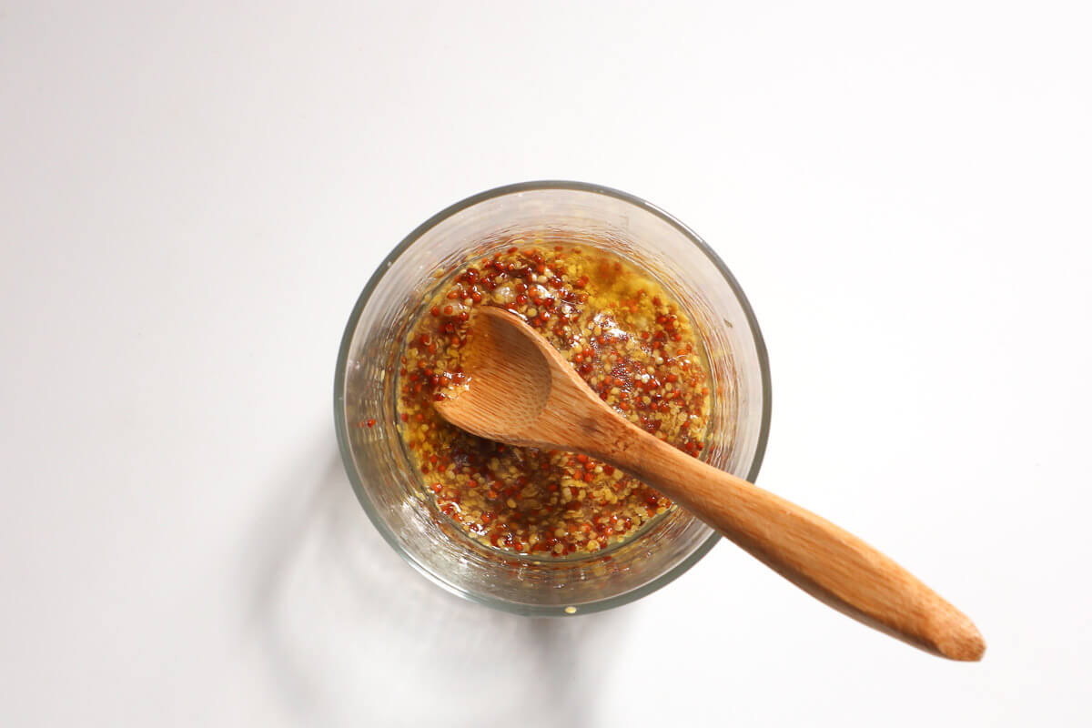 Mustard dressing in glass with wooden spoon in it. 