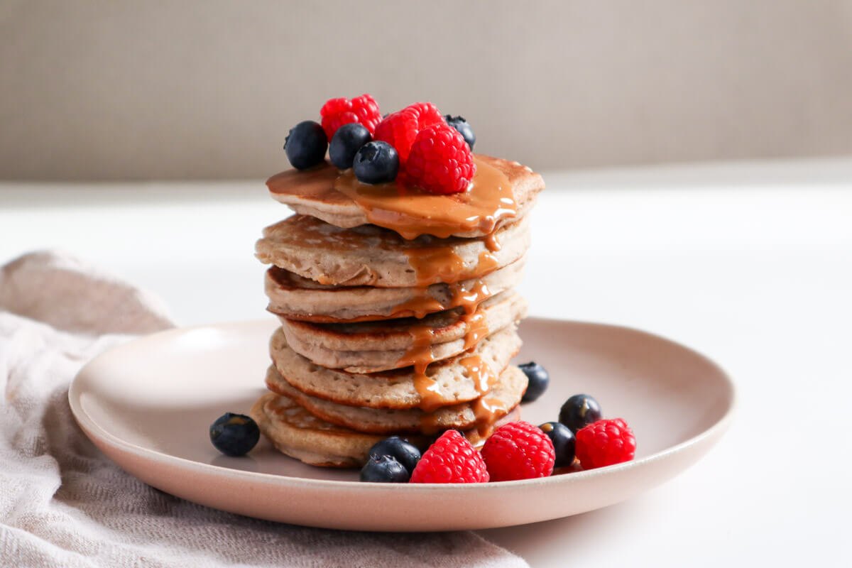 Fluffy Banana Buckwheat Pancakes stacked and topped with fresh fruit and peanut butter.