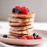 Fluffy Banana Buckwheat Pancakes stacked and topped with fresh fruit and peanut butter.