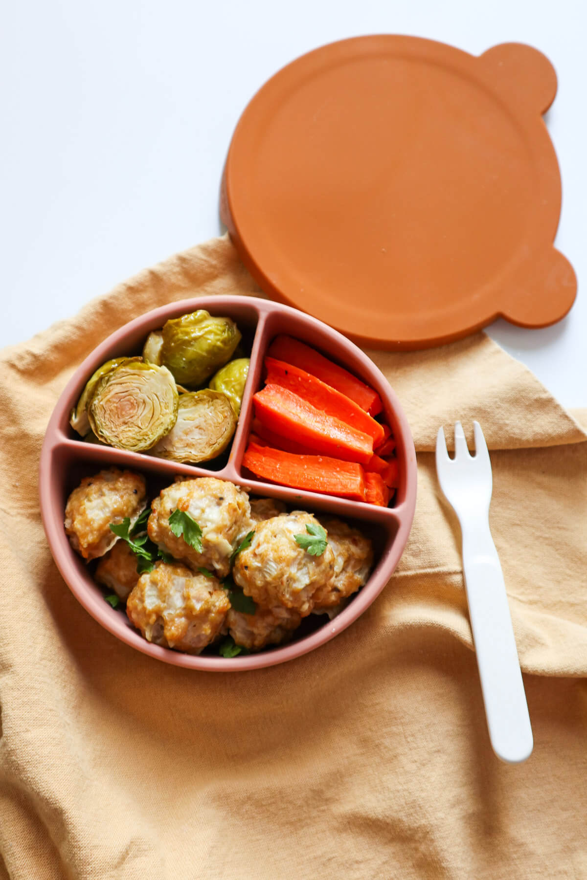 Chicken meatballs in a baby plate with a baby fork next to it.