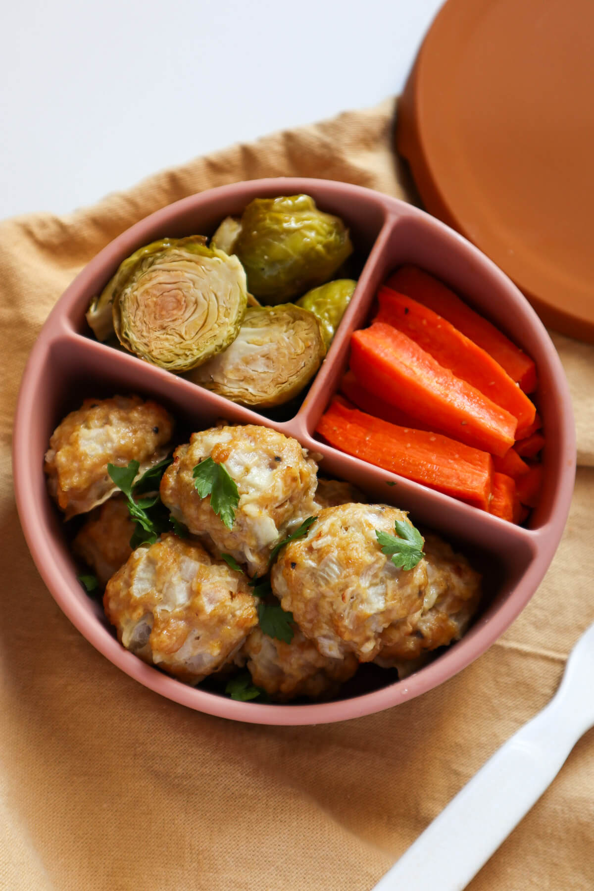 Chicken meatballs for baby in a baby plate with brussel sprouts and carrots. 