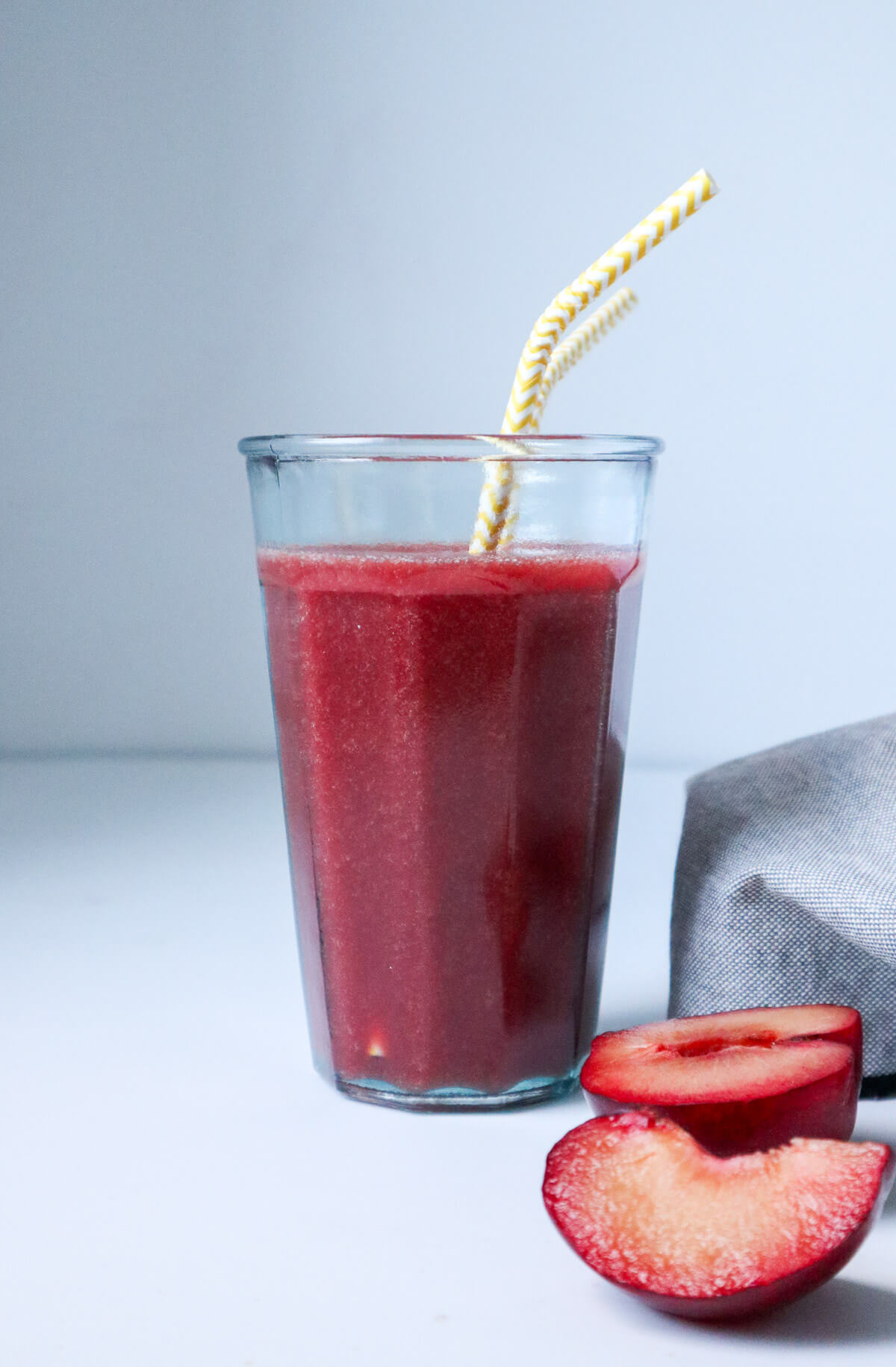 Fresh homemade plum juice drink in a glass with yellow straws.