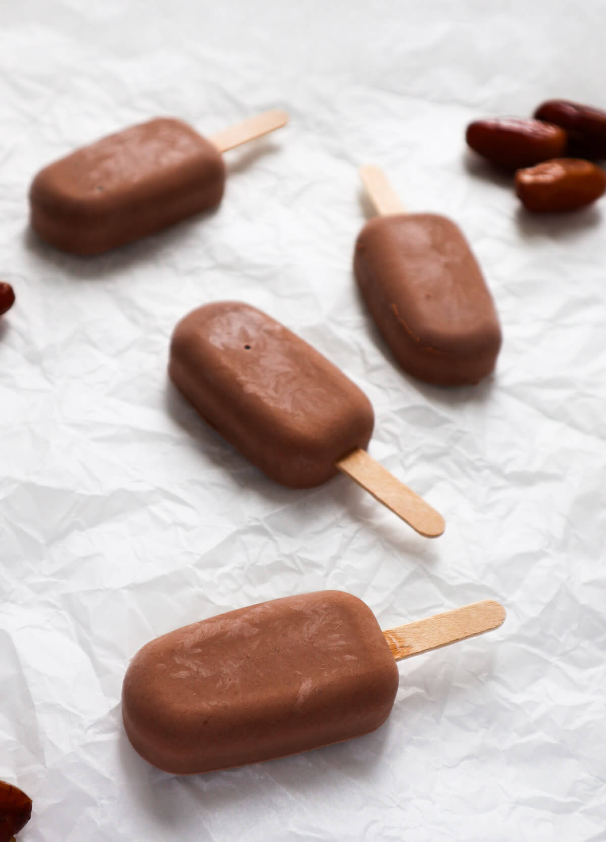 4 healthy yogurt chocolate popsicles on white parchment paper.