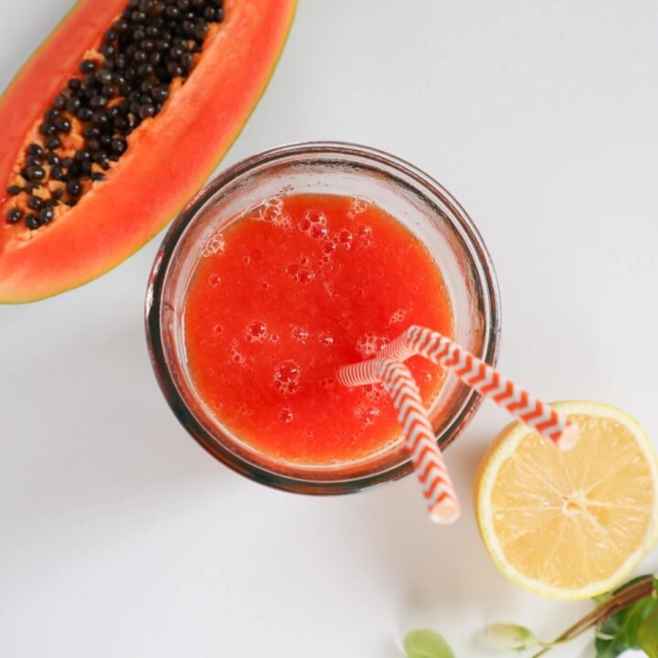 Top down view of papaya juice in a glass next to a lemon.